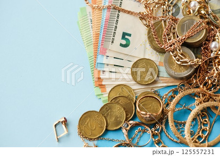 European union Euro money bills and coins with golden rings and jewelry necklaces on blue table European union Euro money bills and coins with golden rings and jewelry necklaces on blue table 125557231