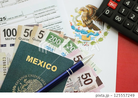 Mexican pesos money bills in big amount lies on table with pen, calculator, passport and tax forms 125557249