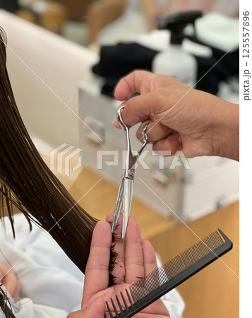 Close up of professional hairstylist using scissors and comb to cut straight wet hair showing precision, craftsmanship and care during a salon haircut service for maintaining healthy hair Close up of professional hairstylist using scissors and comb to cut straight wet hair showing precision, craftsmanship and care during a salon haircut service for maintaining healthy hair 125557896