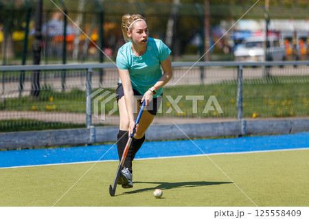 Young sportswoman leading the ball at the field hockey game 125558409