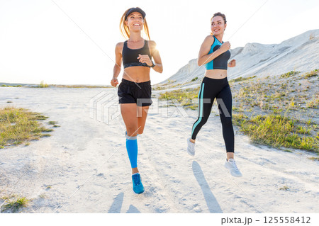 Two athletic woman enjoy outdoor running in sunlight against a scenic backdrop Two athletic woman enjoy outdoor running in sunlight against a scenic backdrop 125558412