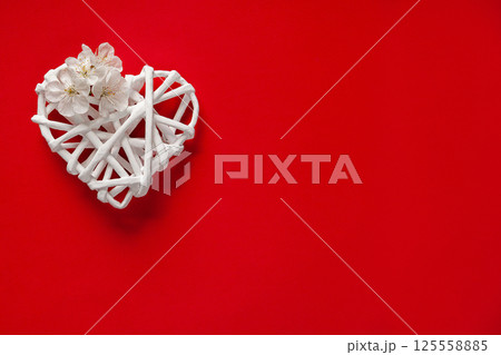 White Wicker Heart Decorated with White Flowers on Bright Red Background 125558885