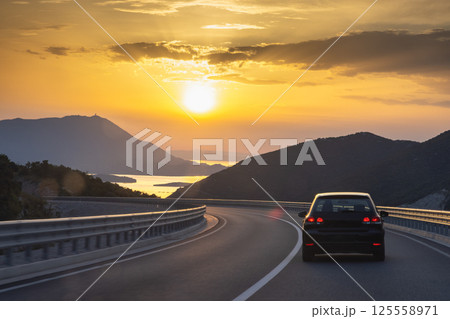 Road on Peljesac peninsula in Croatia, Europe. Scenic Road Trip: Driving into the sunset with mountains and water views on a winding coastal highway. Freedom and adventure awaits! 125558971