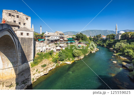 Neretva river near The Old Bridge in Mostar town, Bosnia and Herzegovina, Europe. Scenic view of an old town with a bridge over a river, showcasing historical architecture, serene waters and greenery. 125559025