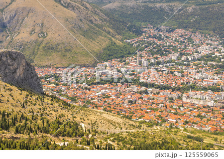 View of Mostar from the Fortica hill, Bosnia and Herzegovina, Europe. Panoramic view of a cityscape nestled in a valley surrounded by mountains, showcasing an urban landscape amidst natural terrain. 125559065