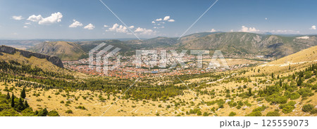 View of Mostar from the Fortica hill, Bosnia and Herzegovina, Europe. Panoramic view of a European city nestled in a valley, surrounded by rugged mountains and clear blue skies. 125559073