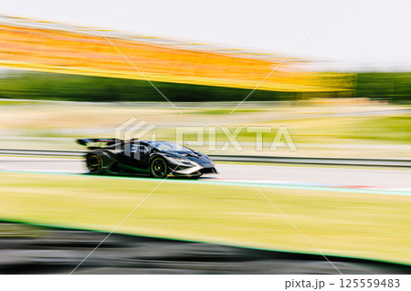 Sports car on circuit, motorsport racing, black car on race track, panning side view 125559483