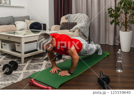 Man doing push-ups on mat in living room workout session Man doing push-ups on mat in living room workout session 125559640