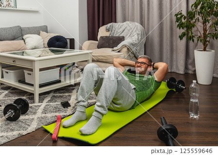 Man exercises at home using a yoga mat and weights 125559646