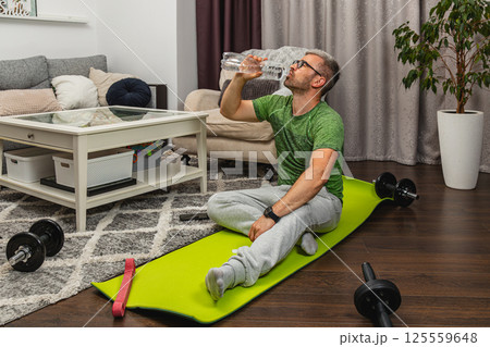 Home workout session featuring a man resting with water Home workout session featuring a man resting with water 125559648