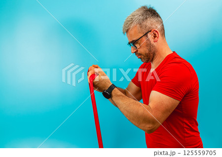 Man exercises with resistance band against blue backdrop 125559705