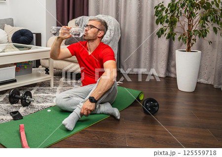 Man exercising at home while taking a water break 125559718