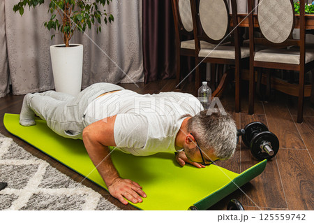 Man exercising with push-ups on a green yoga mat indoors Man exercising with push-ups on a green yoga mat indoors 125559742