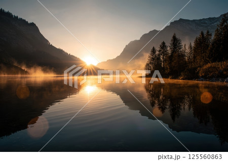Golden Sunrise Over Mountain Lake with Mist and Light Flares in Tranquil Setting 125560863