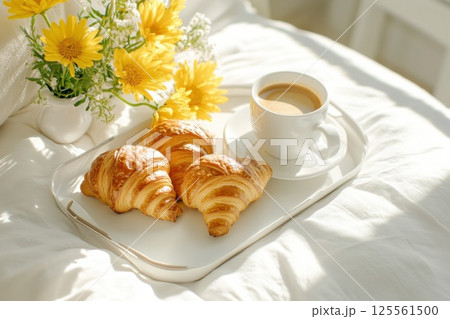 Delightful breakfast tray on a bed featuring croissants coffee and fresh flowers Delightful breakfast tray on a bed featuring croissants coffee and fresh flowers 125561500