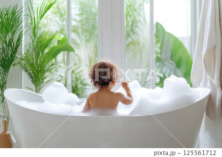 Toddler enjoys bubble bath in bright family bathroom with parental supervision and natural light Toddler enjoys bubble bath in bright family bathroom with parental supervision and natural light 125561712