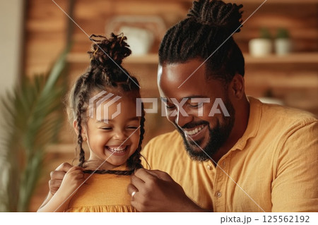 Father braids his young daughters hair in a cozy living room filled with warmth and love 125562192
