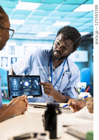 Team of trainee nurses analyzing patient health records during a meeting, utilizing x ray and mri scans with expert physician for a training session. Assistants work with medic. Team of trainee nurses analyzing patient health records during a meeting, utilizing x ray and mri scans with expert physician for a training session. Assistants work with medic. 125563386