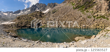 Clear mountain lake reflecting rugged cliffs and snow capped peaks in alpine landscape 125563527