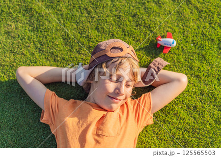 Boy wearing a pilot hat running through the grass with a toy airplane, dreaming of adventures. Childhood, imagination, and freedom concept 125565503