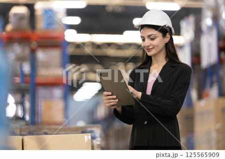 Female uses digital tablet checking stock goods working in logistics. Women professional warehouse worker wearing safety uniform and white hard hat inspect product at storage. Female uses digital tablet checking stock goods working in logistics. Women professional warehouse worker wearing safety uniform and white hard hat inspect product at storage. 125565909