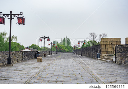 Scenic pathway along ancient city wall lined with traditional lanterns and lush greenery 125569535