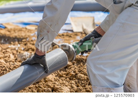 ディスクグラインダーで下水道配管のバリを取る土木作業員 125570903
