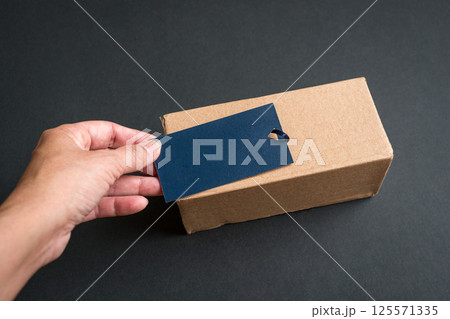 Hand putting a blue tag on top of cardboard parcel. Hand putting a blue tag on top of cardboard parcel. 125571335