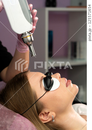 Esthetician aligns laser device over eyebrow for tattoo removal 125571654