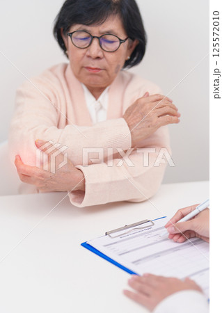Elderly Woman having elbow ache and consulting doctor in hospital. muscle pain due to lateral epicondylitis or tennis elbow. injury, Health and medical consultation concept 125572010