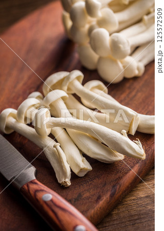 Raw white shimeji mushrooms on wooden cutting board. Raw white shimeji mushrooms on wooden cutting board. 125572509
