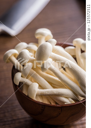 Raw white shimeji mushrooms in bowl on wooden table. Raw white shimeji mushrooms in bowl on wooden table. 125572511