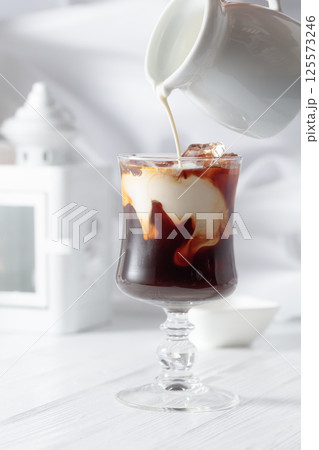 Cream is poured into a glass with iced coffee. 125573246
