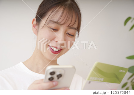 通帳とスマホを見てほほえむ女性 125575844