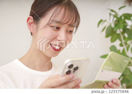 スマホと通帳を見てほほえむ女性 スマホと通帳を見てほほえむ女性 125575846