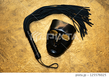 Adult sex games. Kinky lifestyle. Mask and whip ridding crop on the golden background. Bdsm outfit Adult sex games. Kinky lifestyle. Mask and whip ridding crop on the golden background. Bdsm outfit 125576025