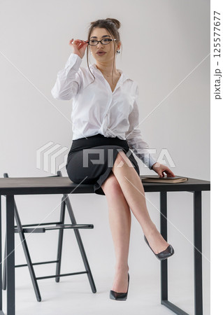 Young Caucasian businesswoman adjusting glasses while sitting on desk in office setting 125577677