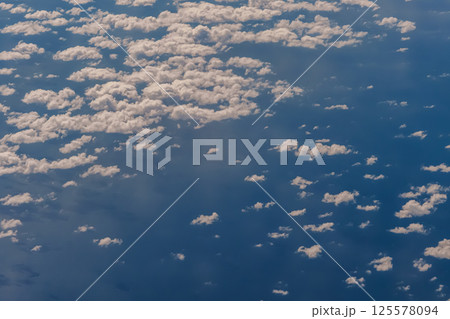 Aerial view from airplane window above green ground. View from the airplane window with beautiful clouds at sunrise. Earth and sky as seen through window of an airplane. 125578094