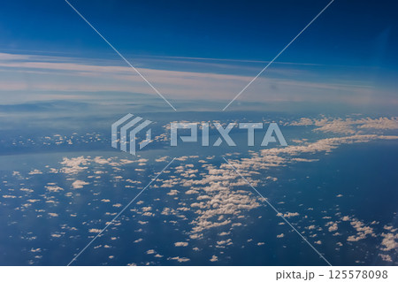 Aerial view from airplane window above green ground. View from the airplane window with beautiful clouds at sunrise. Earth and sky as seen through window of an airplane. Aerial view from airplane window above green ground. View from the airplane window with beautiful clouds at sunrise. Earth and sky as seen through window of an airplane. 125578098