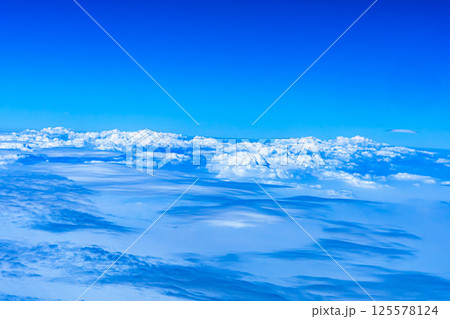 Aerial view from airplane window above green ground. View from the airplane window with beautiful clouds at sunrise. Earth and sky as seen through window of an airplane. 125578124