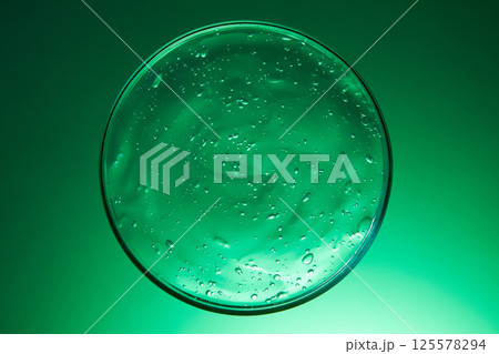 Close-up photo of cosmetic essence extracted from natural ingredients. The essence texture is transparent, with many air bubbles. The essence dish display on a green background. Laboratory concept. Close-up photo of cosmetic essence extracted from natural ingredients. The essence texture is transparent, with many air bubbles. The essence dish display on a green background. Laboratory concept. 125578294