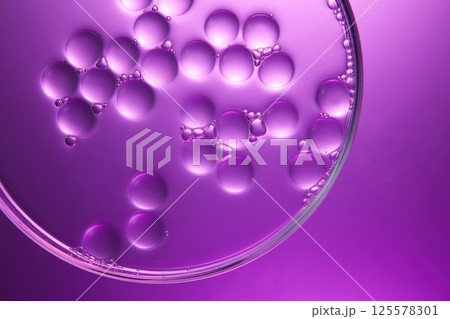 A petri dish containing simulated particles of cosmetic solution. Molecular structures swatch in the shape of a sphere, with some tiny bubbles around. Laboratory concept with dark purple background. A petri dish containing simulated particles of cosmetic solution. Molecular structures swatch in the shape of a sphere, with some tiny bubbles around. Laboratory concept with dark purple background. 125578301