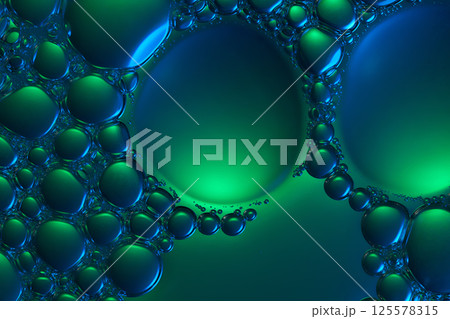 The essence drops onto the neon green background, forming two large bubbles, surrounded by countless other tiny bubbles clinging to the edges. Close-up of molecules in a cosmetic essence. The essence drops onto the neon green background, forming two large bubbles, surrounded by countless other tiny bubbles clinging to the edges. Close-up of molecules in a cosmetic essence. 125578315