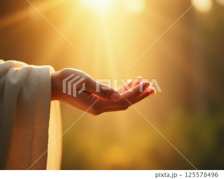 Outstretched hand in white robe reaching toward golden sunlight, symbolizing faith and hope. 125578496