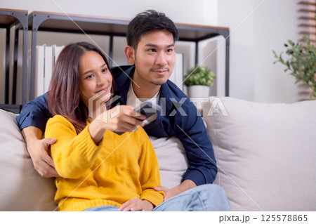 Happy young asian couple sitting on cozy sofa watching TV together and enjoying a relaxation. Happy young asian couple sitting on cozy sofa watching TV together and enjoying a relaxation. 125578865