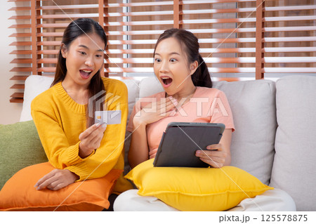 Two young asian woman sitting on sofa using tablet computer shopping online with credit card. Two young asian woman sitting on sofa using tablet computer shopping online with credit card. 125578875