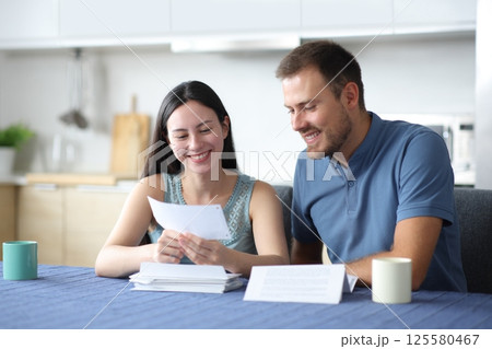 Happy interracial couple holding bank statement Happy interracial couple holding bank statement 125580467