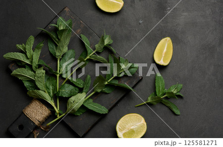 Whole and cut limes with fresh mint leaves arranged on a dark textured surface. 125581271