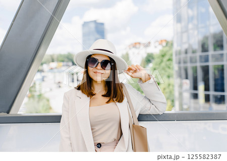 Beautiful brunette businesswoman wearing suit and white hat, walking on the street. 125582387