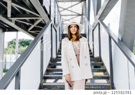 Beautiful brunette businesswoman wearing suit and white hat, walking on the street. Beautiful brunette businesswoman wearing suit and white hat, walking on the street. 125582391